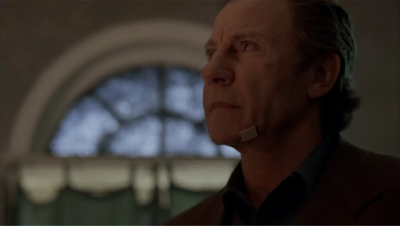 Ajuste de Cuentas (2016) movie still: medium — A dimly lit room features a large arched window with curtains in the background. A man stands in the…