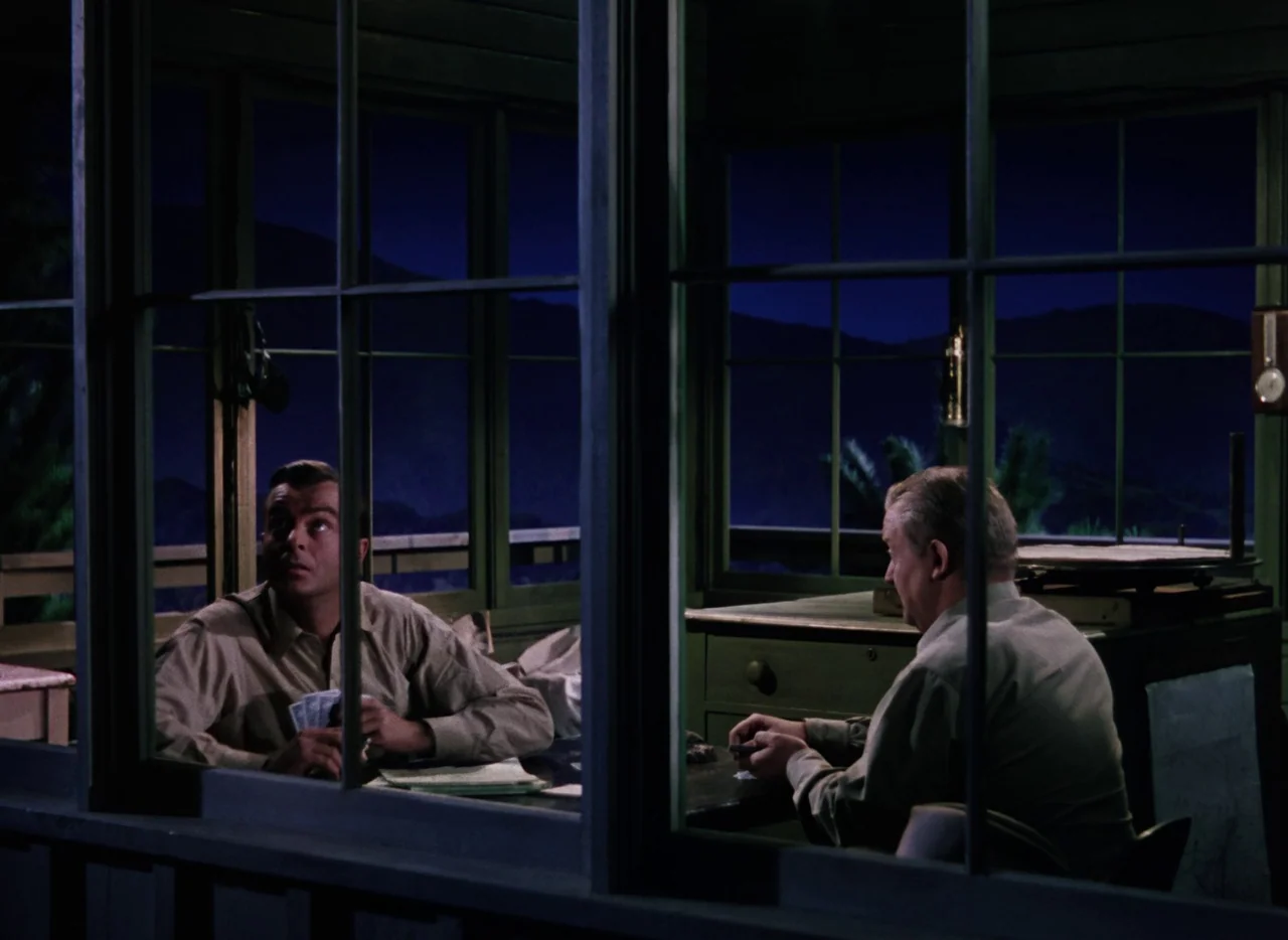 The War of the Worlds (1953) movie still: medium — A rustic wood-frame fire lookout tower at night offers views of distant dark mountains. Two men…