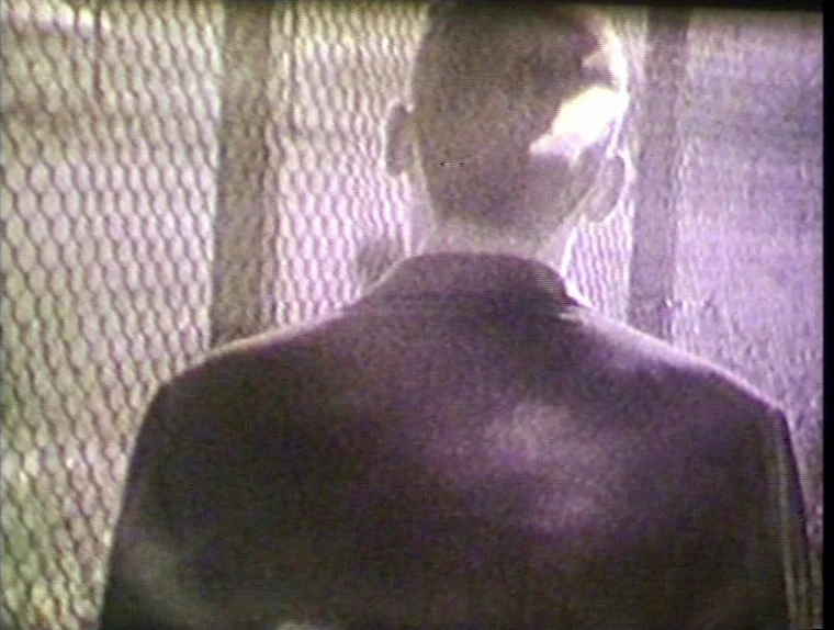 The Angelic Conversation (1985) movie still: medium — A figure stands in front of a chain link fence at night. The footage displays significant VHS…
