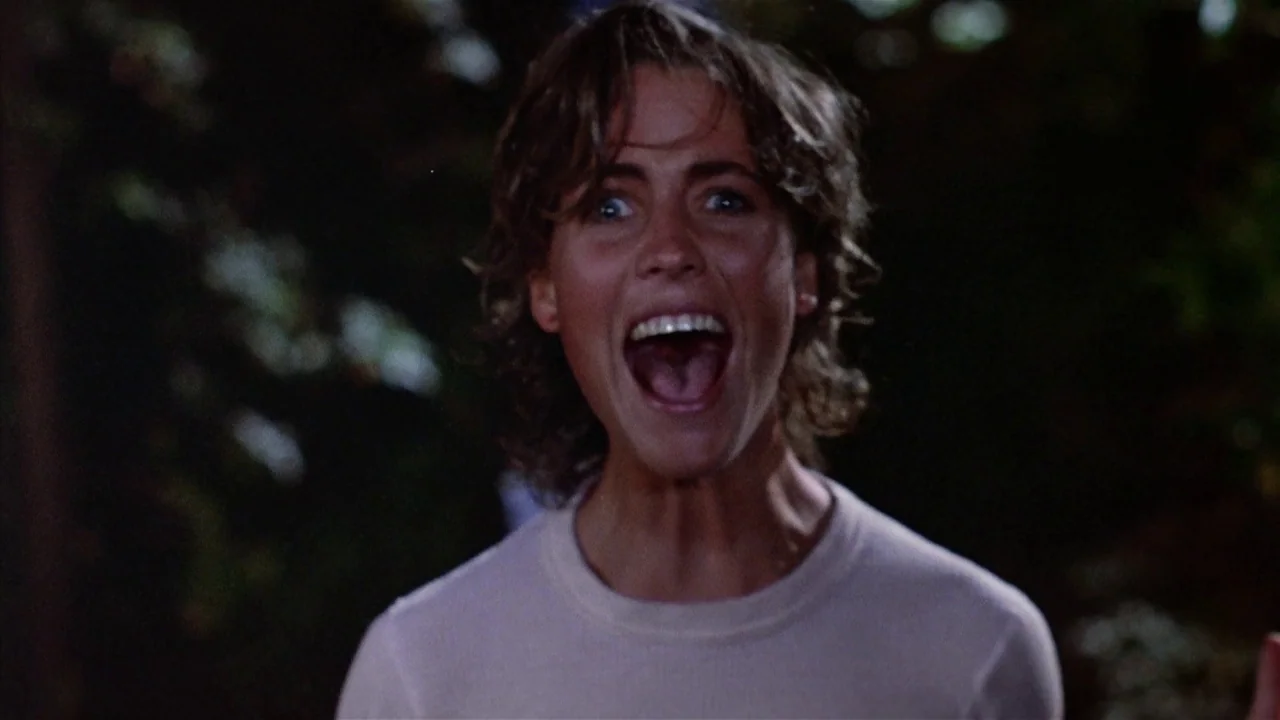 Friday the 13th Part 2 (1981) movie still: closeup — A woman stands in a dark wooded area at night. She has her mouth wide open in a scream.