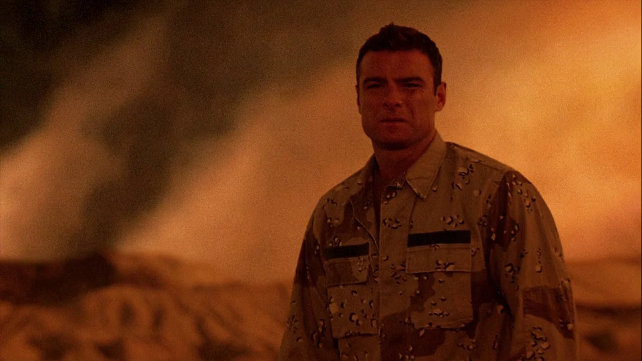 The Manchurian Candidate (2004) movie still: medium — A soldier stands in a dark desert environment with a massive, out-of-focus fire behind. The…