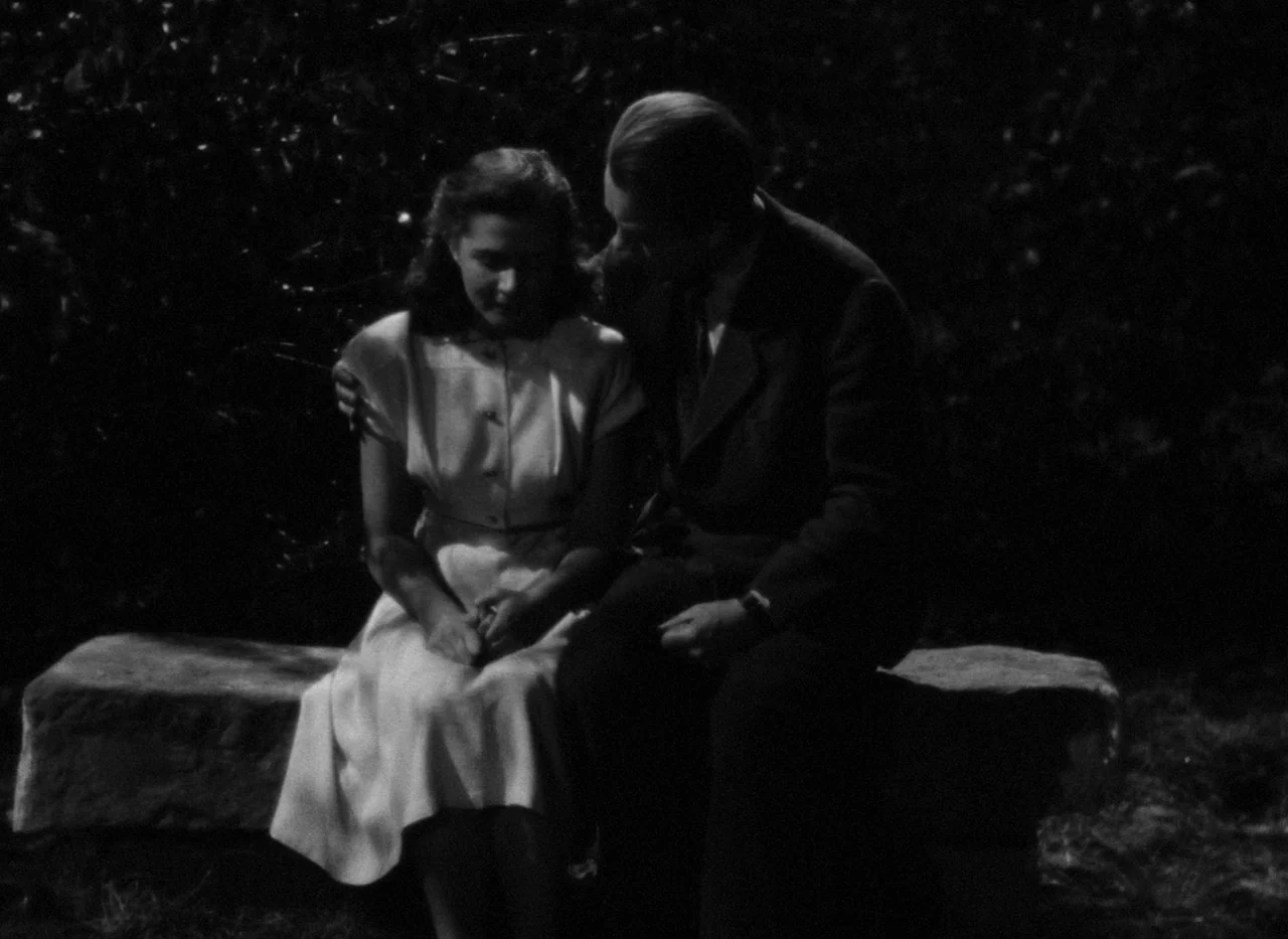 Krakatit (1948) movie still: medium — A dark outdoor setting featuring a stone bench surrounded by deep shadows and vegetation. A man and a woman…