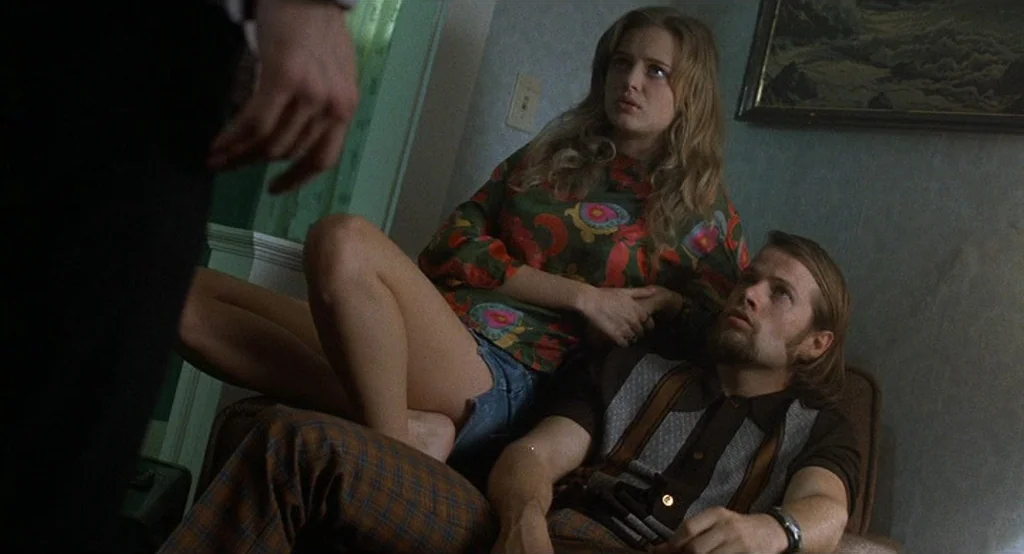 Drugstore Cowboy (1989) movie still: medium — A living room interior featuring patterned walls, a framed landscape painting, and vintage furniture.…