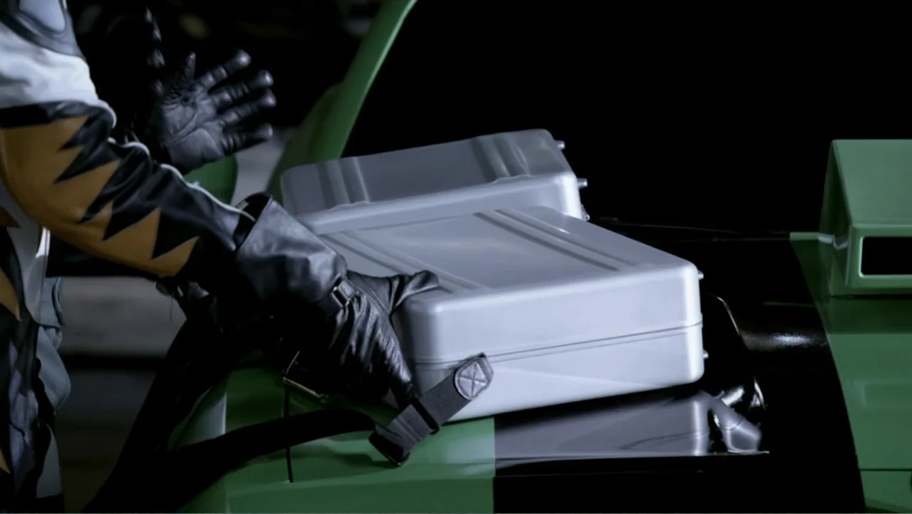 Ben 10: Race Against Time (2008) movie still: medium — A dark, dimly lit garage interior features a green vehicle with black racing stripes. A…