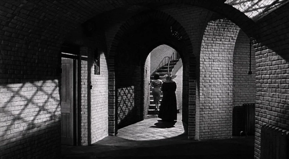 Suddenly, Last Summer (1959) movie still: wide — A stone corridor constructed with curved brick arches and a tiled floor. Two women walk away from…