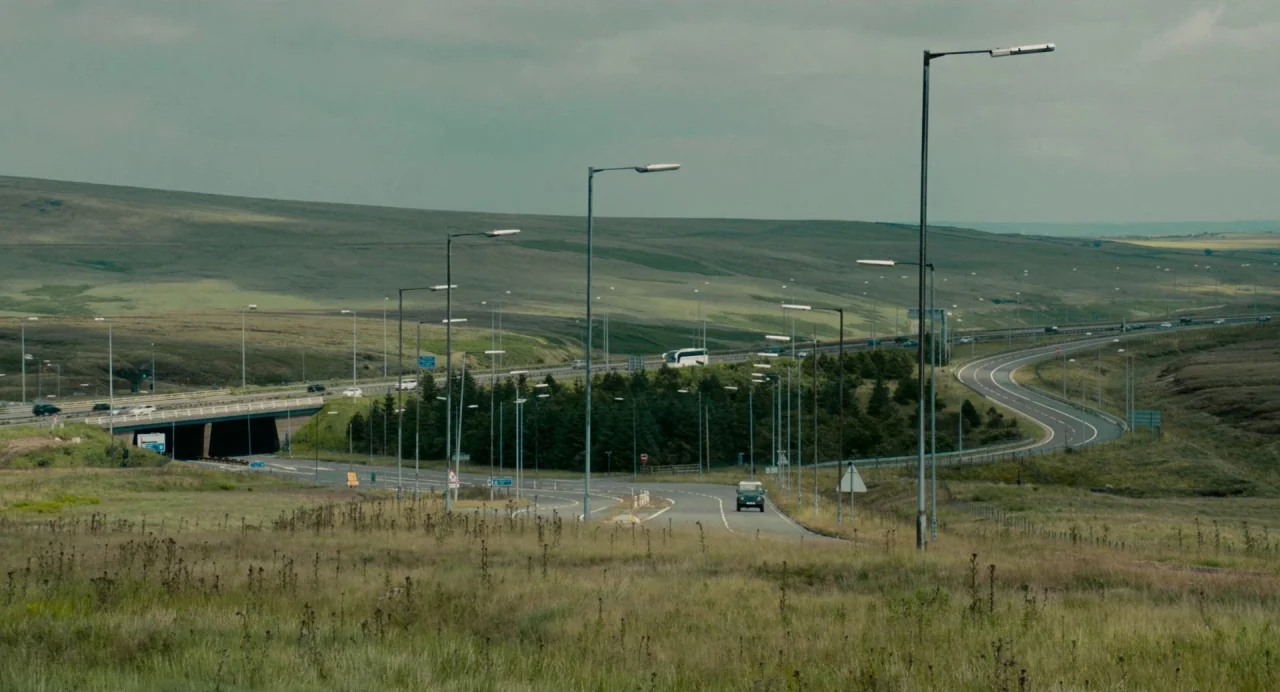 Dark River (2017) movie still: establishing — A winding multi-lane highway cuts through an expansive, rolling landscape covered in dry grass.…