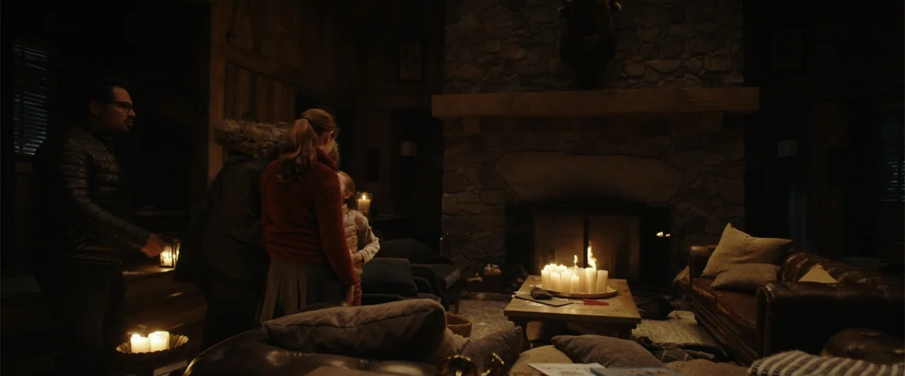 Moonfall (2022) movie still: medium — A dark wooden lodge room features a large stone fireplace with a buffalo head mounted. Three people stand…
