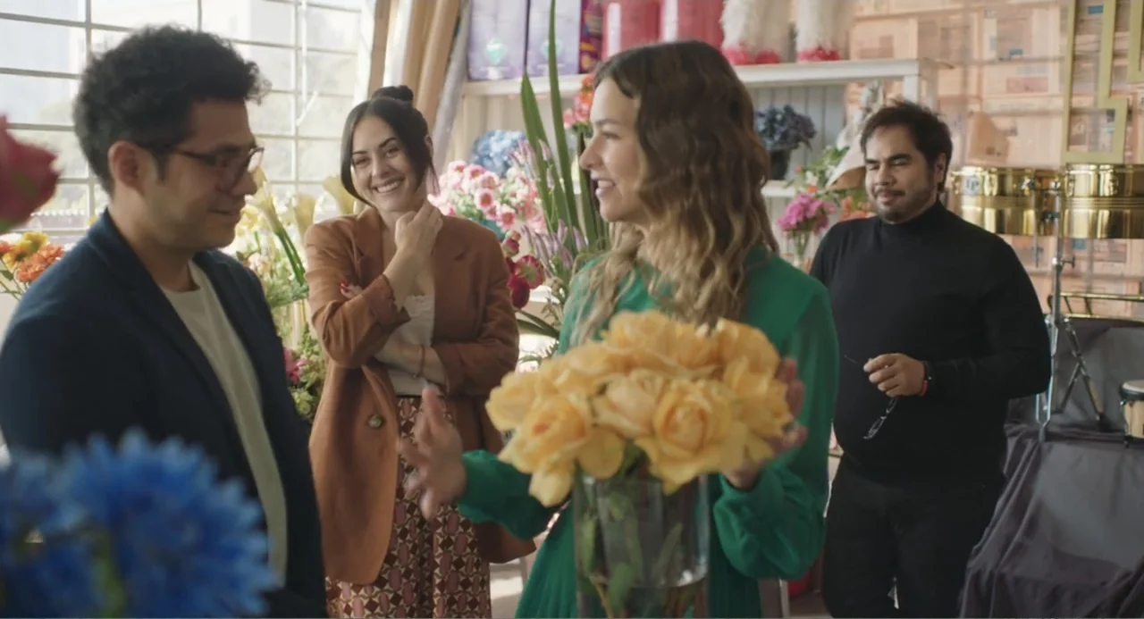 Casando a mi Ex (2023) movie still: medium — A sunlit flower shop with shelves of bouquets and instruments in the background. A group of four adults…