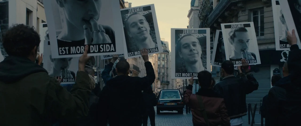 BPM (Beats Per Minute) (2017) movie still: medium — A group of people walk down a cobblestone city street during a protest demonstration. They hold…