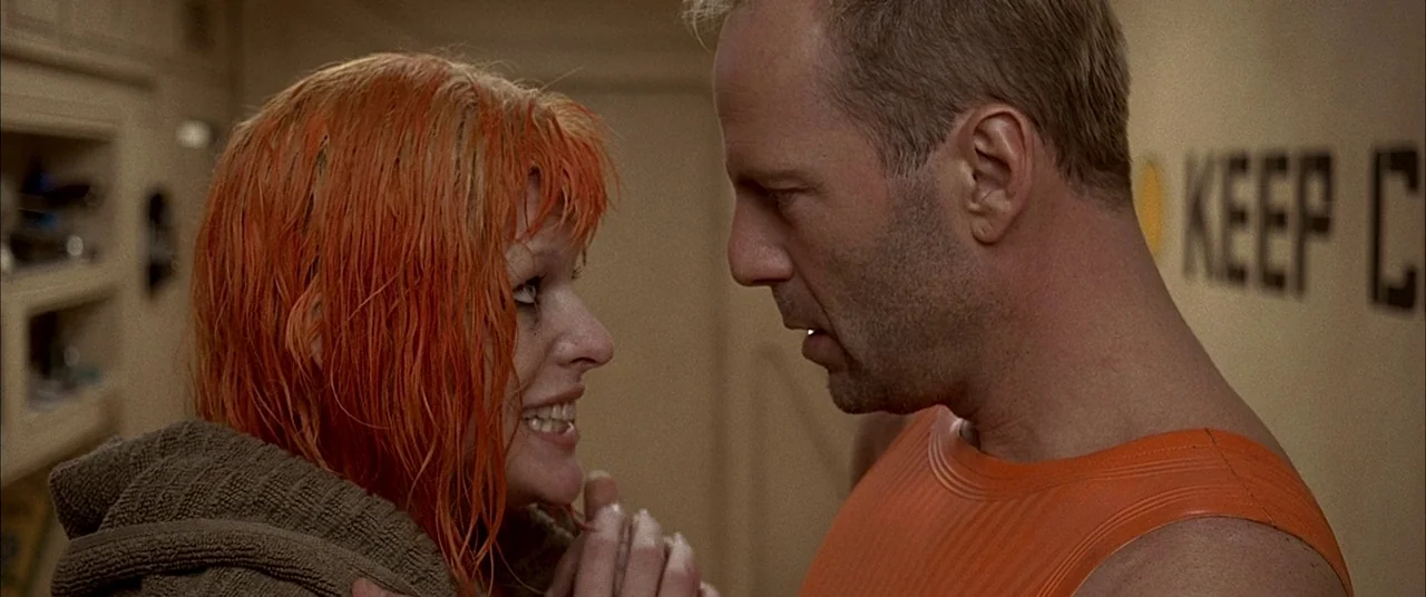 The Fifth Element (1997) movie still: medium — A sterile, off-white corridor wall with black lettering reads KEEP C. A man faces a woman with wet…