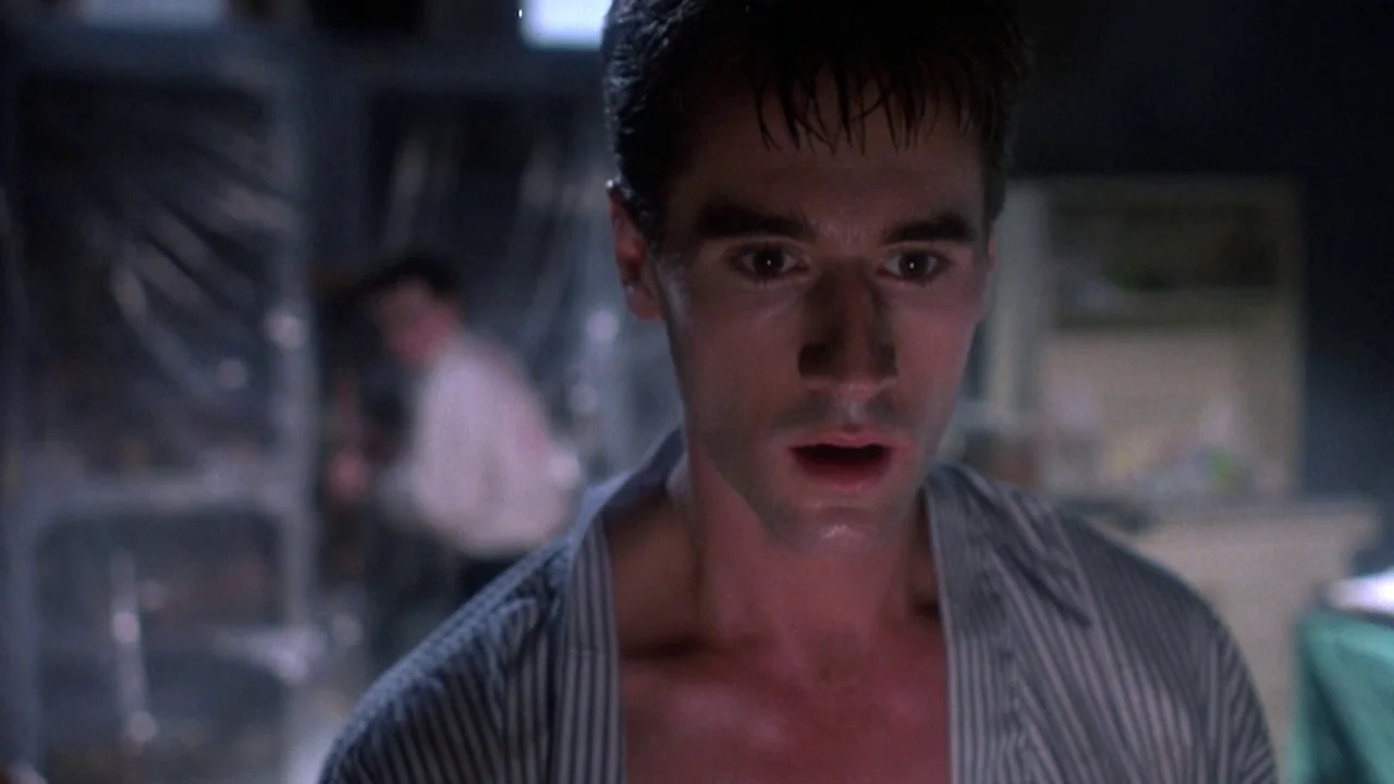 Re-Animator (1985) movie still: closeup — A dimly lit room contains plastic-covered equipment and metallic surfaces in the blurred background. A…
