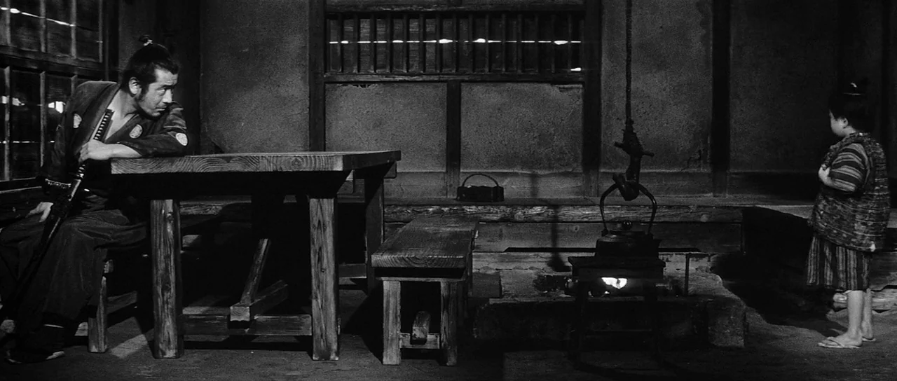 Yojimbo (1961) movie still: wide — A dark, wood-paneled traditional Japanese room features a central recessed fire pit. A samurai sits at a table…