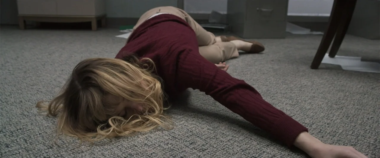 Office Uprising (2018) movie still: medium — An office interior features a gray carpet floor with metal filing cabinets nearby. A woman in a maroon…