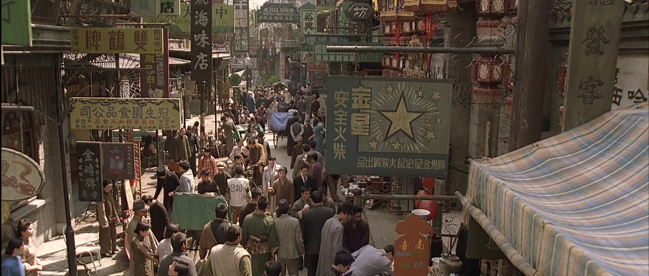Ip Man (2008) movie still: establishing — A crowded 1940s market street is filled with numerous vendors, shoppers, and hanging signs. Pedestrians…
