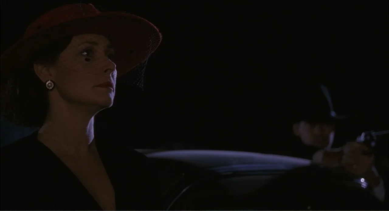 Wild Orchid II: Two Shades of Blue (1991) movie still: medium — A dark night setting features a woman in a red hat in the foreground. A man holding…