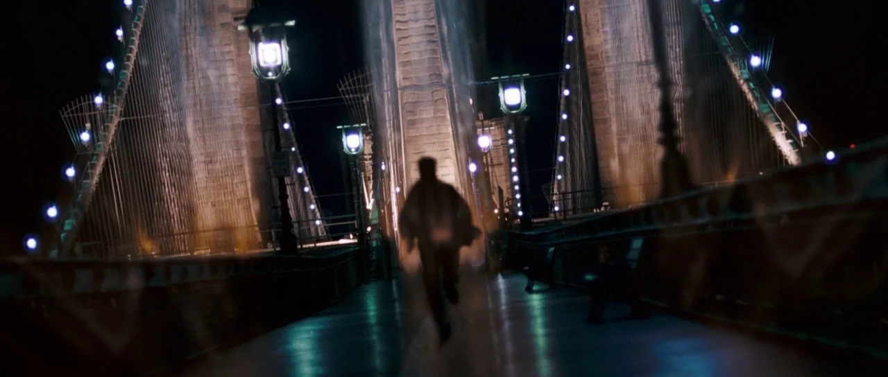 Stay (2005) movie still: fullbody — A man runs along the pedestrian walkway of a suspension bridge at night. The bridge towers rise up in the…