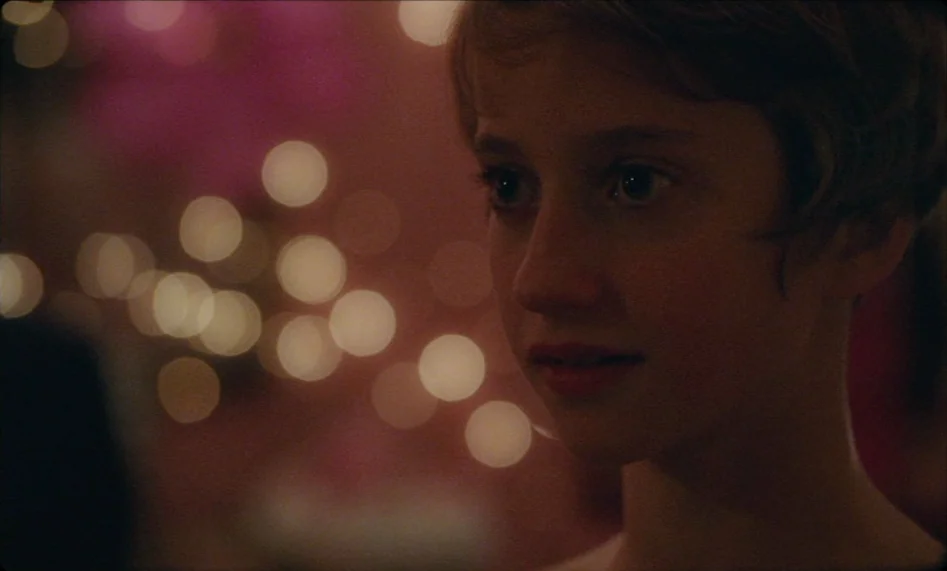 Misunderstood (2014) movie still: closeup — A dimly lit indoor space with bright circular out-of-focus lights in the background. A teenage girl with…