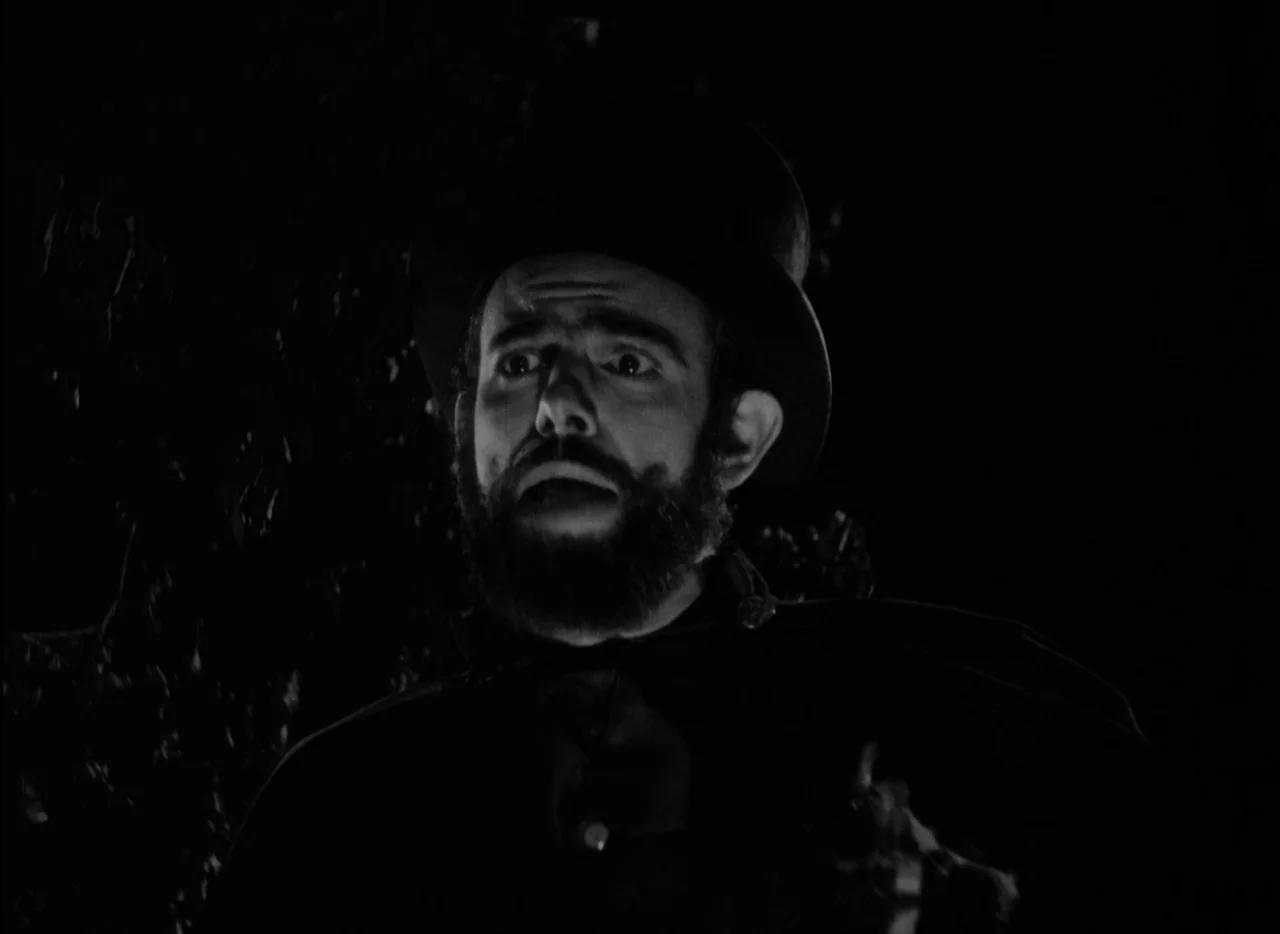 At Midnight I’ll Take Your Soul (1964) movie still: closeup — A man stands in darkness surrounded by dense foliage at night. He looks up while…