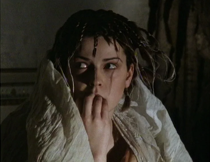 The Tempest (1979) movie still: closeup — A dark indoor space with minimal background detail visible behind the subject. A young woman with braided…