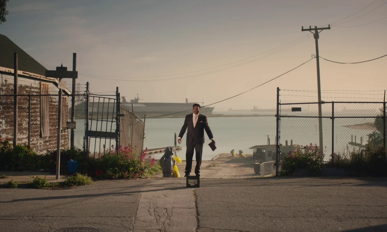 The Last Black Man in San Francisco (2019) movie still: fullbody — A paved path leads to a fence overlooking a waterfront harbor area. A man stands…