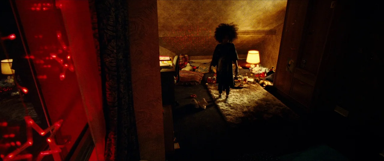 The Five Devils (2022) movie still: fullbody — A cluttered attic space is filled with toys, blankets, and a wooden wardrobe. A person stands in the…