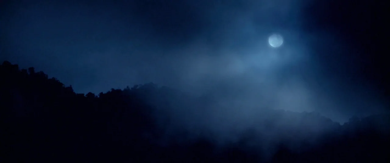 Harriet movie still: establishing — A night landscape features a dark mountain silhouette partially obscured by low-hanging fog. A bright full moon…
