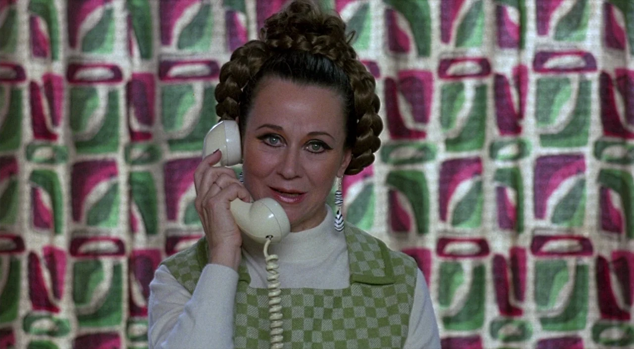 Women on the Verge of a Nervous Breakdown (1988) movie still: closeup — A woman stands before a wall with a vibrant pink and green geometric…