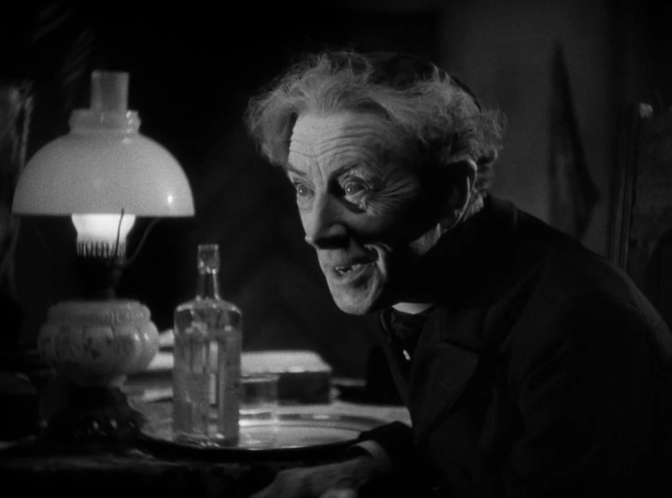 The Bride of Frankenstein (1935) movie still: medium — A dimly lit interior space is dominated by a man sitting near a lamp. An oil lamp sits on the…