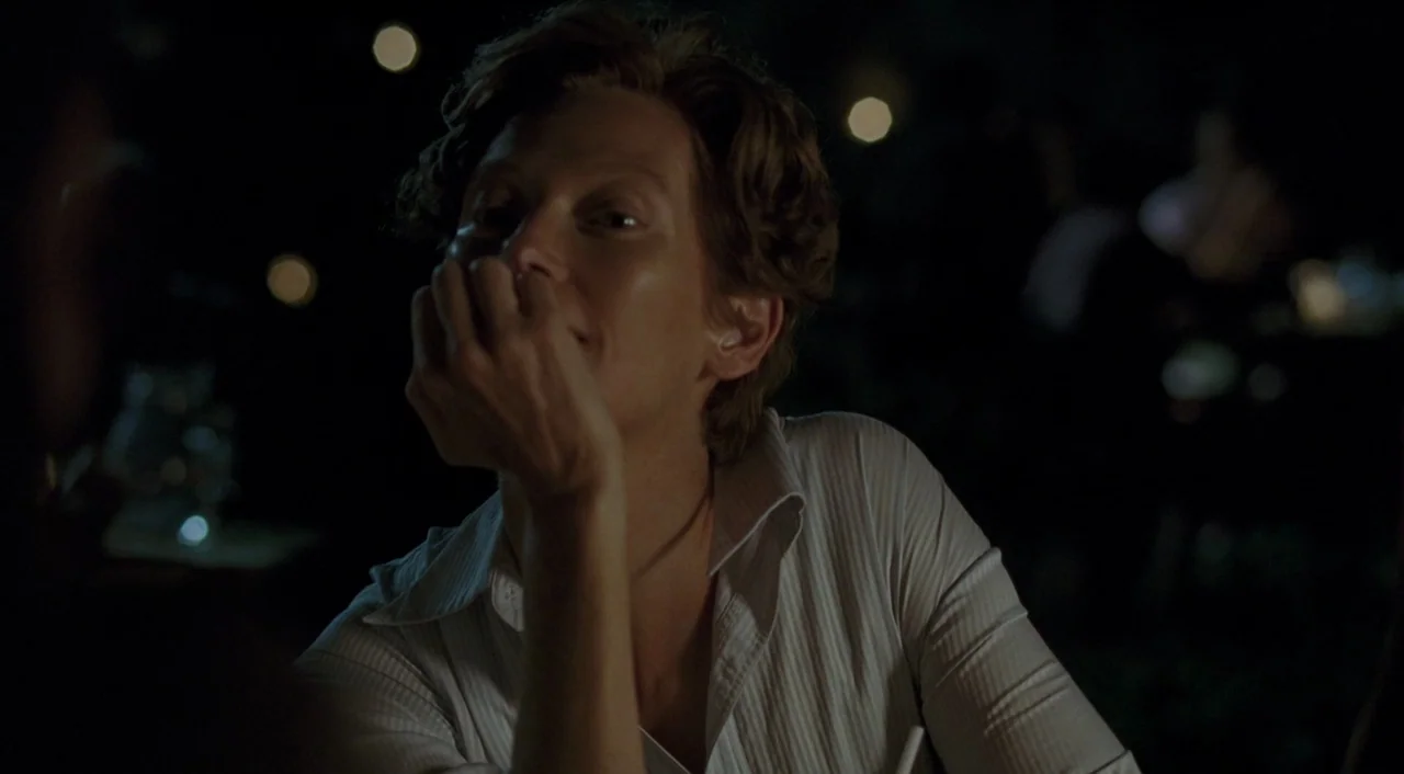 A Bigger Splash (2015) movie still: medium — An interior space is dimly lit by distant, out-of-focus light sources. A woman with short hair rests…