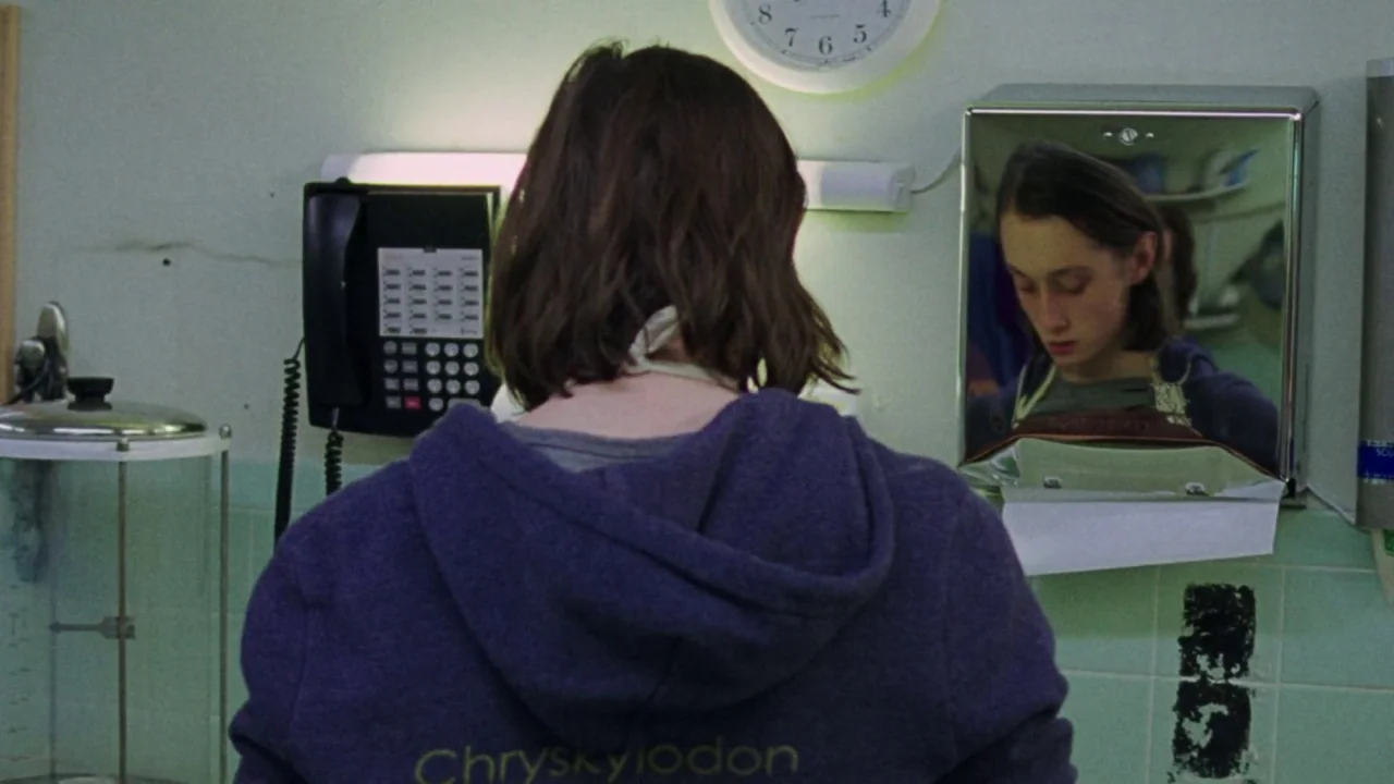 I Am Not a Serial Killer (2016) movie still: medium — A utilitarian office break room with light green tiled walls and a wall clock. A young woman…