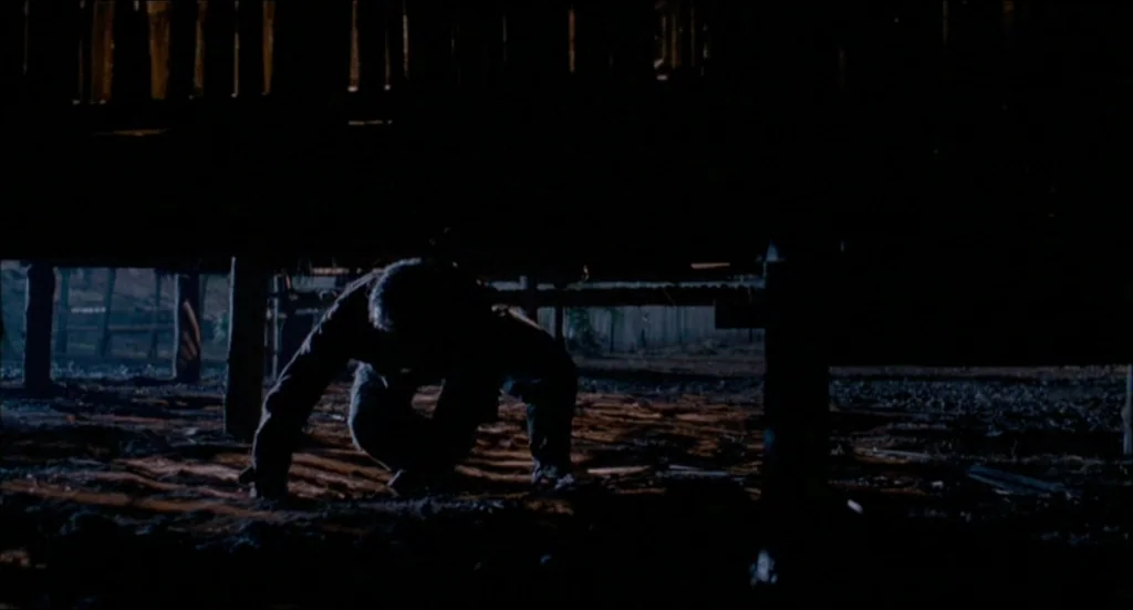 Rescue Dawn movie still: medium — The dark, cramped dirt area beneath a wooden elevated building at night. A lone figure moves cautiously on hands…