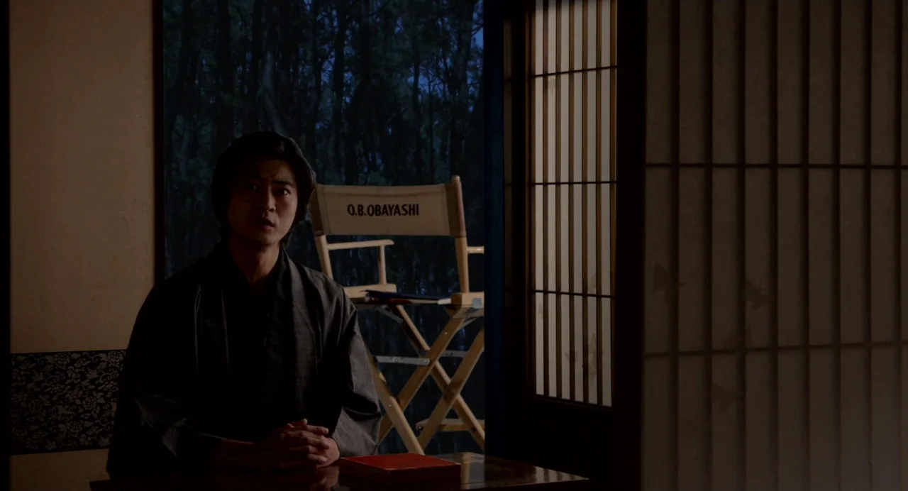 Hanagatami movie still: medium — A dark indoor space featuring traditional Japanese sliding doors and a director's chair behind. A man in a kimono…