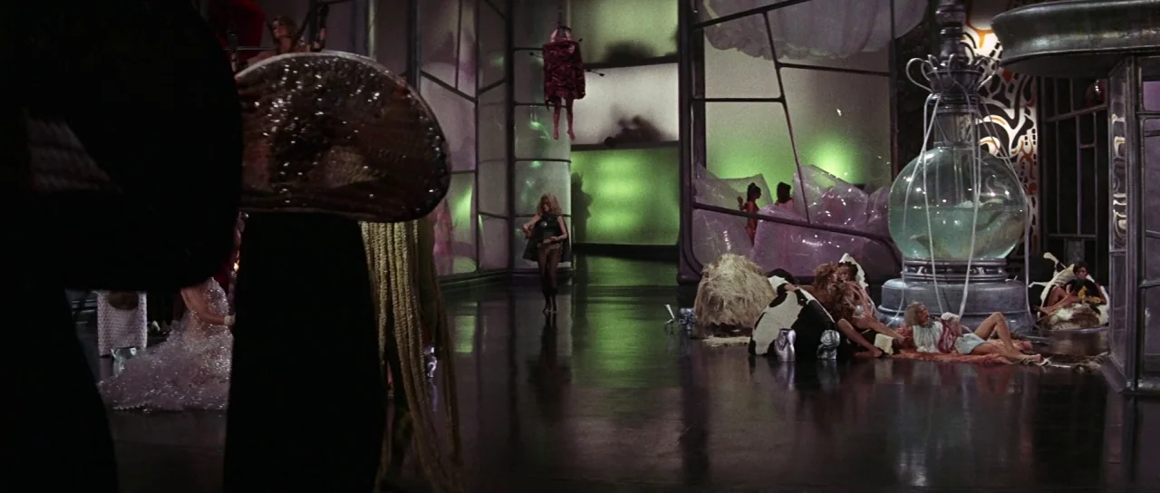 Barbarella (1968) movie still: wide — A futuristic laboratory features glass partitions and large glass liquid containers on pedestals. A blonde…
