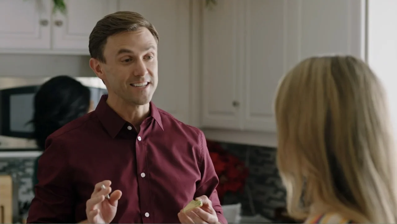 Ghosts of Christmas Past (2021) movie still: medium — A well-lit residential kitchen features white cabinetry and a dark tiled backsplash. A man in…