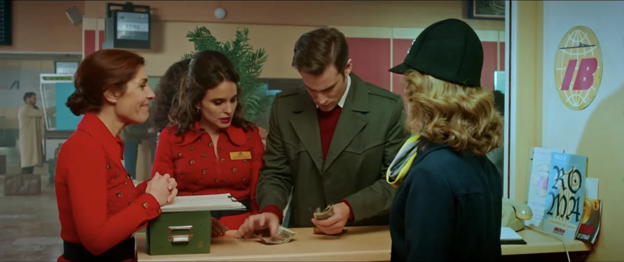 My Heart Goes Boom! (2020) movie still: medium — An airline counter features travel posters and administrative paperwork on the desk. Three airline…