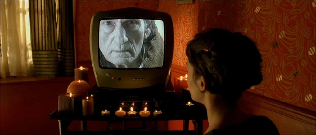 Amelie (2001) movie still: medium — A dark room with warm-toned patterned wallpaper is lit by numerous glowing candles. A woman viewed from behind…