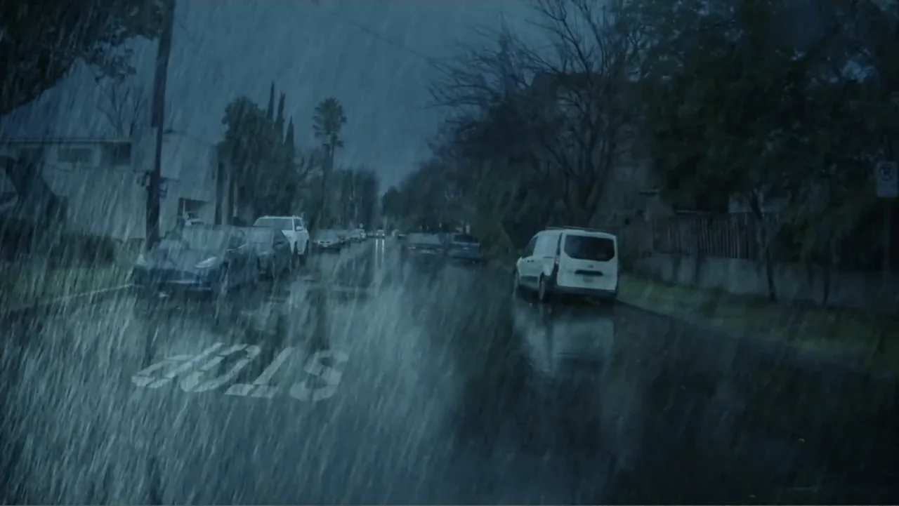 Storm Damage (2000) movie still: establishing — A dark residential suburban street during a heavy rainstorm at night. Multiple parked cars line the…