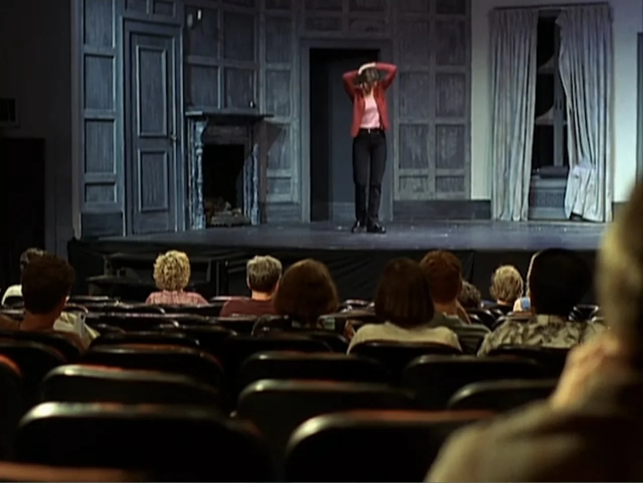 Catch a Falling Star (2000) movie still: wide — A theatrical stage features dark wood paneling with a fireplace and white curtains. A woman in a red…