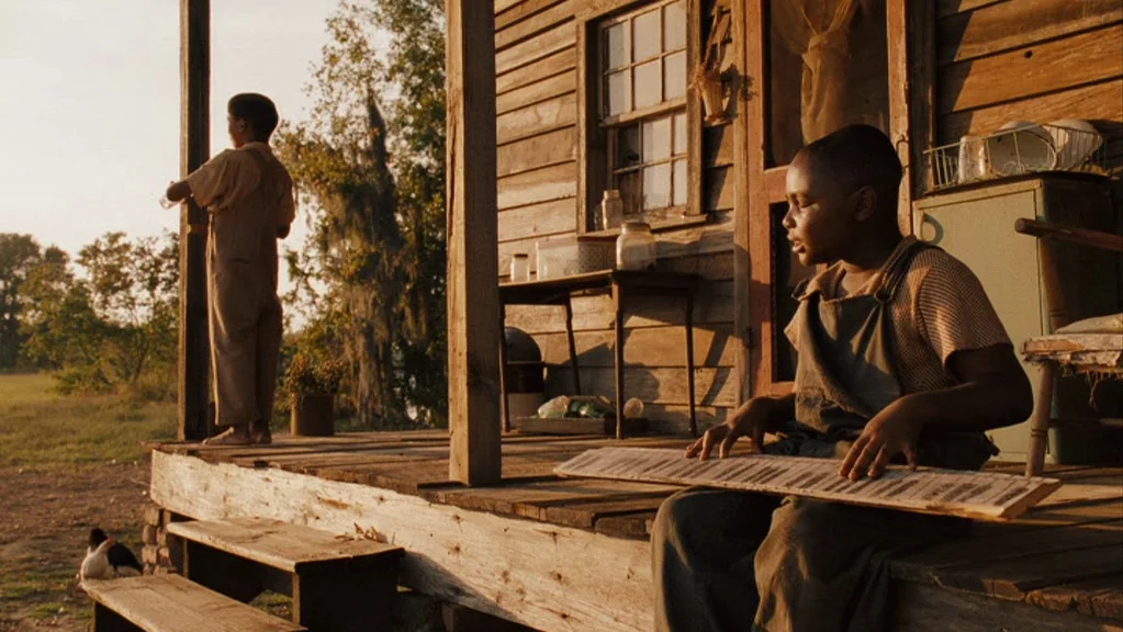 Honeydripper (2007) movie still: medium — A rural wooden house features a weathered porch with a dirt yard visible beyond. Two young boys in…