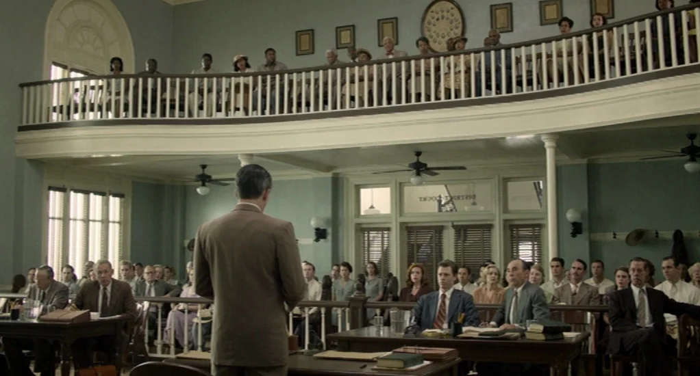 Free State of Jones (2016) movie still: wide — A spacious, pale green historical room with a mezzanine level filled with seated spectators. A man in…