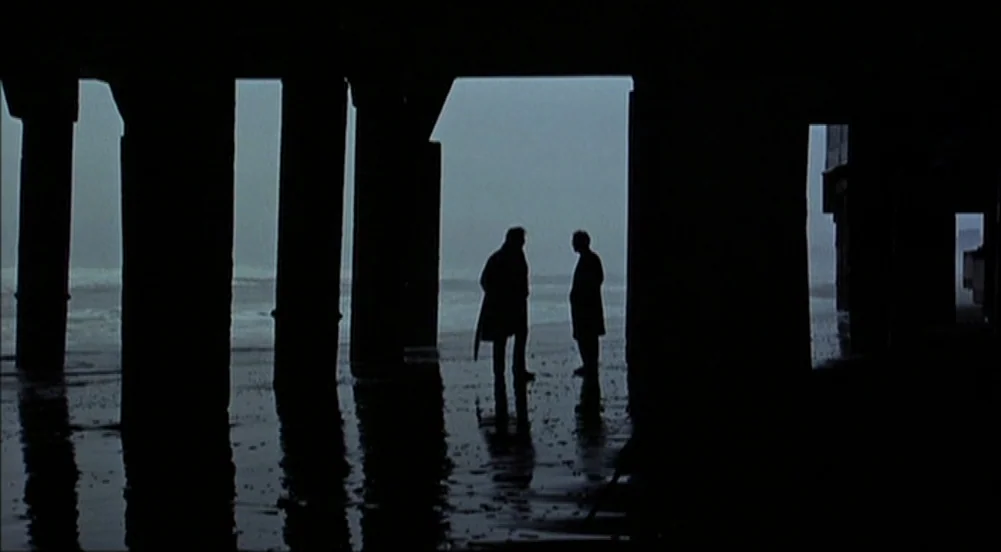 The King Of Marvin Gardens movie still: wide — Two figures stand under the dark structure of a pier facing the open ocean. They are silhouetted…