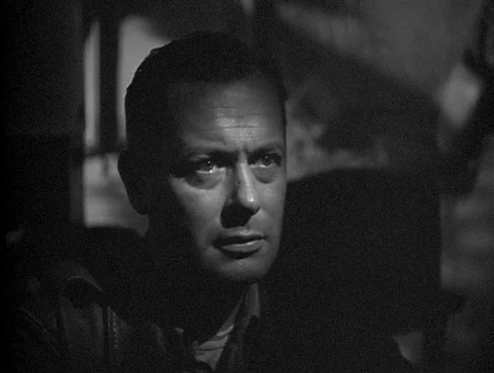 They Were Expendable (1945) movie still: closeup — An interior space is dimly lit by a sharp side light. A man with short dark hair is framed in a…