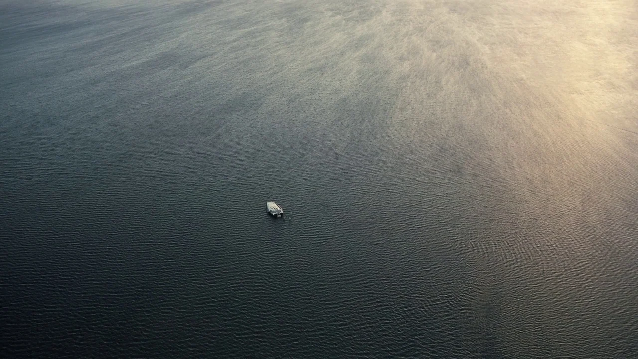 Interstellar (2014) movie still: establishing — An aerial view looks down over a dark, rippling body of water at sunset. A small white boat is…