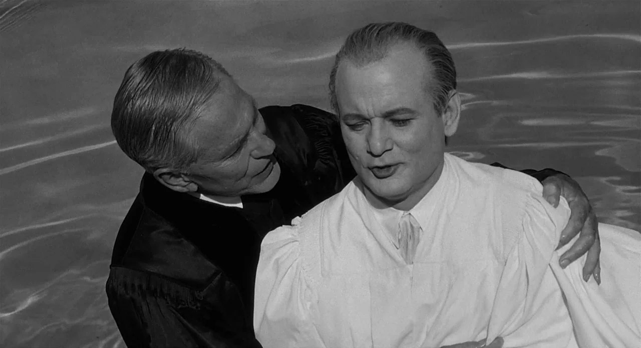 Ed Wood (1994) movie still: medium — Two men stand in water during a baptismal ceremony in an outdoor setting. The older man stabilizes the younger…