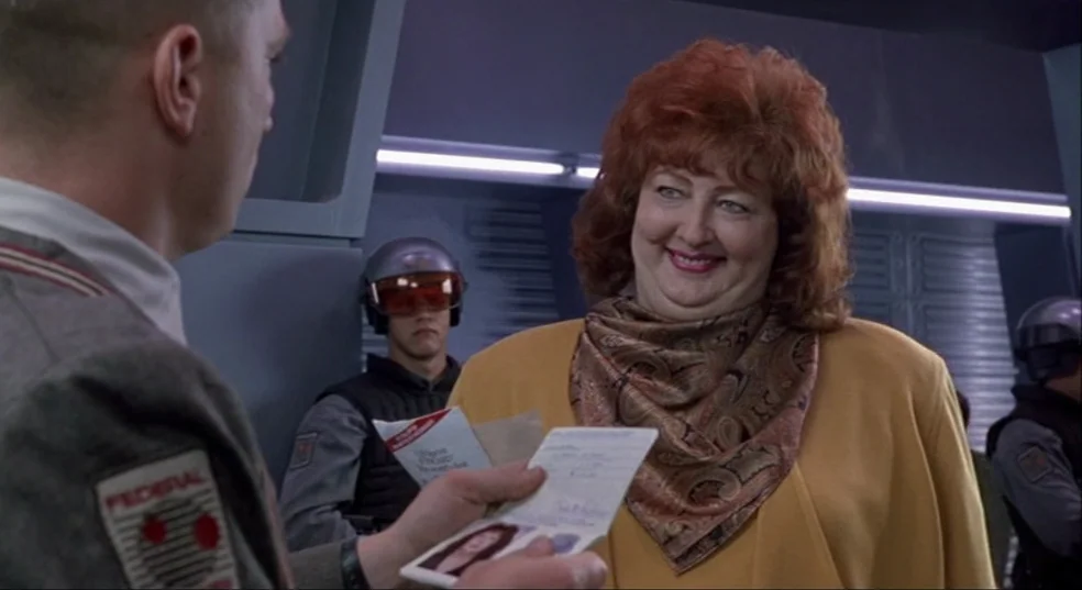 Total Recall (1990) movie still: medium — A futuristic transit terminal with metallic walls and integrated white lighting strips. A woman smiles as…