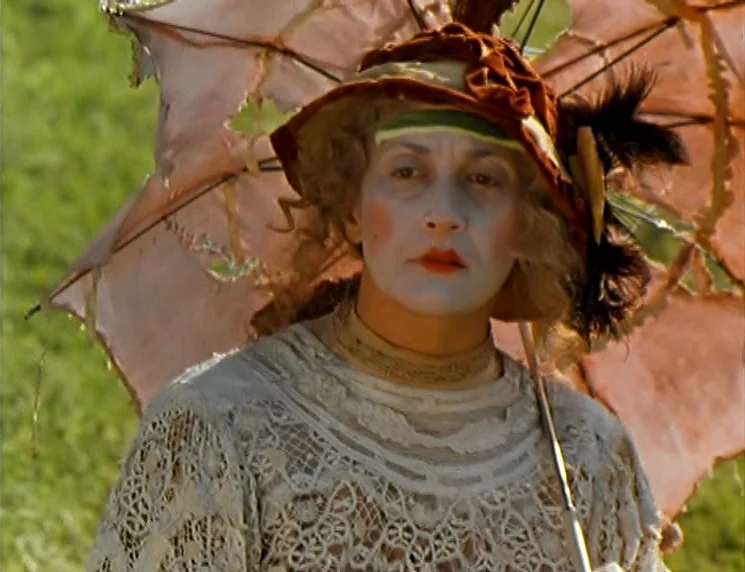 The Wishing Tree (1977) movie still: medium — An individual stands in a bright green field under a tattered, peach-colored lace parasol. The subject…