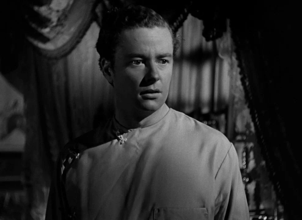 The Magnificent Ambersons (1942) movie still: medium — A dimly lit room features draped fabric and obscured structural details in the background. A…