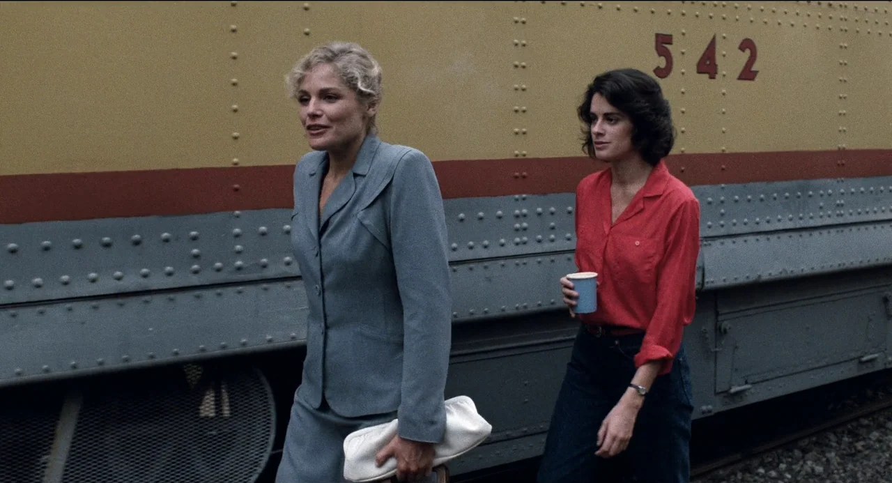 Desert Hearts (1985) movie still: medium — Two women walk past a yellow train locomotive with a prominent number 542 painted. The train car has…