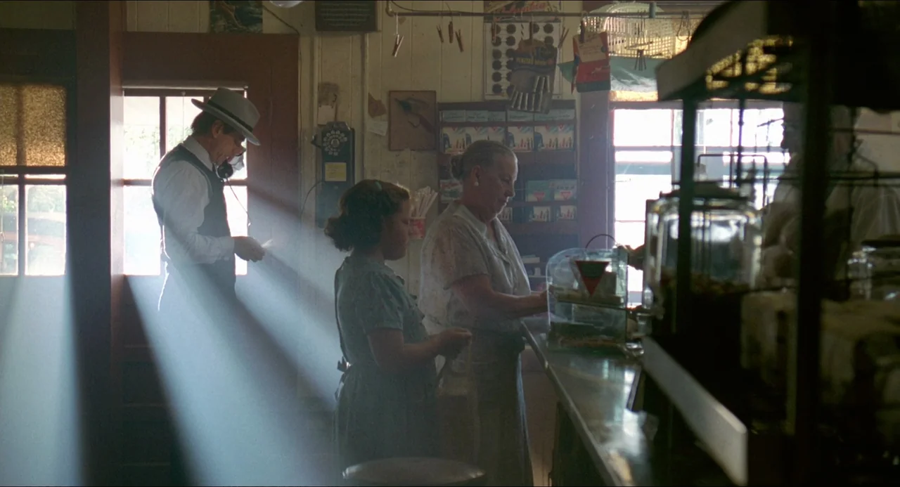Lolita (1997) movie still: medium — A dimly lit 1940s general store interior contains wooden shelves and a service counter. A man speaks on a…
