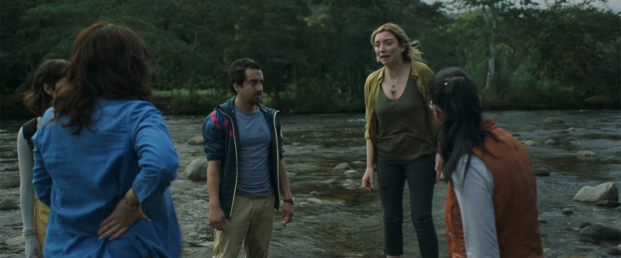 Mirreyes contra Godínez 2: El retiro (2022) movie still: medium — A shallow rocky river runs through a dense green wooded area during the day. Four…
